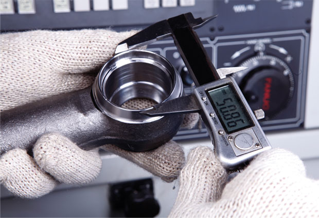 Gloved hands measuring an automotive component with a digital caliper